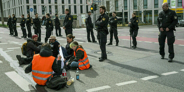 Demonstrierende die auf dem Boden sitzen, blockieren eine Kreuzung, Polizisten stehen im Hintergrund