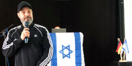 Ben Salomo am Mikrofon mit israelischer Flagge im Hintergrund