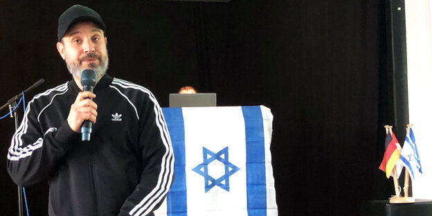 Ben Solomon am microfoon met Israëlische vlag op de achtergrond