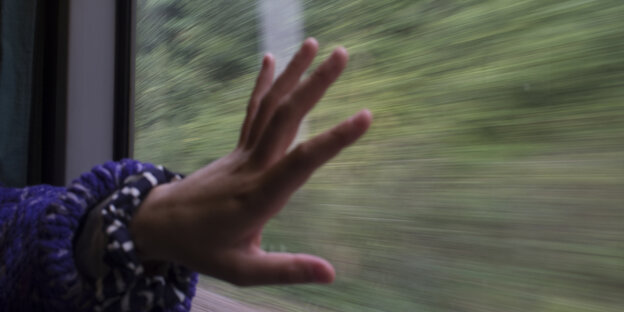 Eine Person in einem fahrenden Zug hält eine seiner Hände ans Zugfenster.