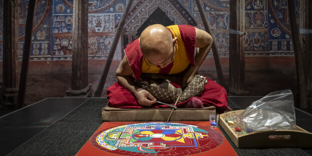 Ein Mönch arbeitet an einem Mandala aus farbigem Sand