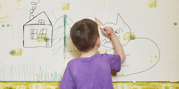 Ein Junge bemalt mit Buntstiften eine tapezierte Wand