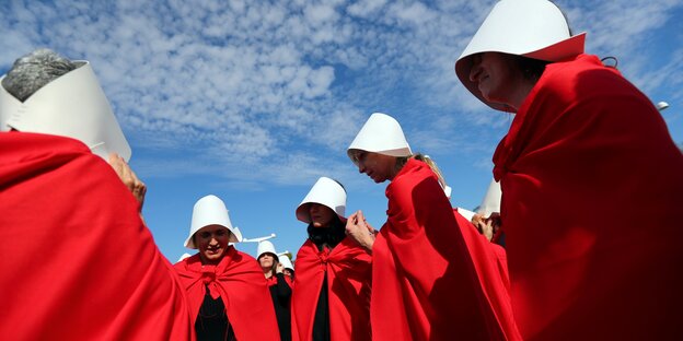 Das Foto zeigt eine Gruppe von Frauen mit weißen Kapuzen und roten Mänteln nach der Serie 