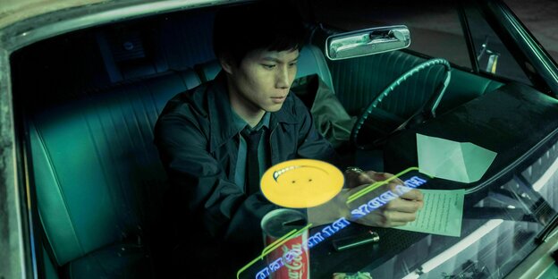 Ein junger Mann sitzt in einem Auto und notiert sich etwas auf einem Zettel