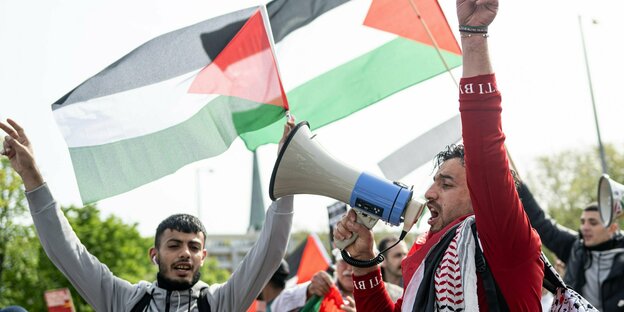 Zwei Demonstranten mit Megaphon vor palästinensischen Flaggen