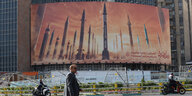 Auf einer Werbetafel in Teheran stehen Raketen aufgereiht. Davor geht ein Mann vorbei.
