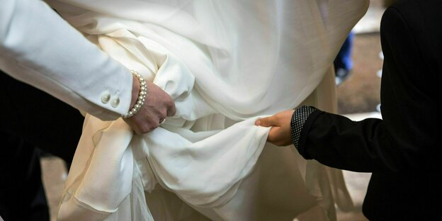 Zwei Hände an einem Hochzeitskleid