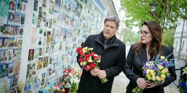 Ein Mann und eine Frau halten Blumen in der Hand und gehen in Kiew an einer Mauer entlang