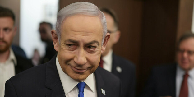 Benjamin Netanyahu, der Premierminister Israels. Er ist ein alter Mann mit grauen Haaren. Sein Kopf ist leicht geneigt. Er lächelt.