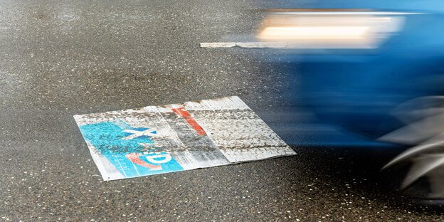 Ein AfD-Wahlplakat auf der Straße, über die ein Auto fuhr