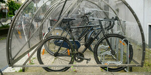 In einer abschließbaren und durchsichtigen Fahrradbox vor einem Wohnhaus stehen Fahrräder.