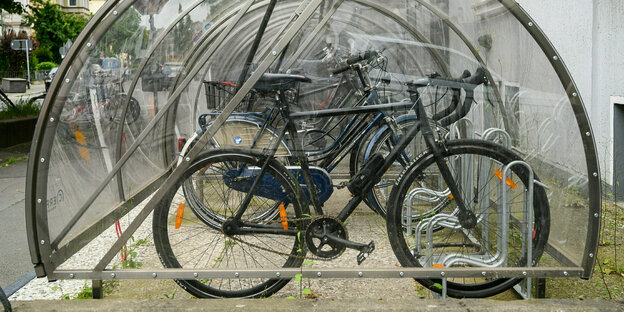 Fahrräder werden in einer abschließbaren und transparenten Fahrradbox vor einem Wohnhaus aufbewahrt.