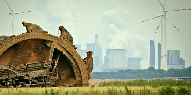 Ein Braunkohlebagger gräbt im Tagebau Garzweiler, im Hintergrund ist ein Kraftwerk hinter Windrädern zu sehen