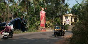 Fahrzeuge fahren an einer übergroßen Darstellung einer Frau im Sari vorbei.