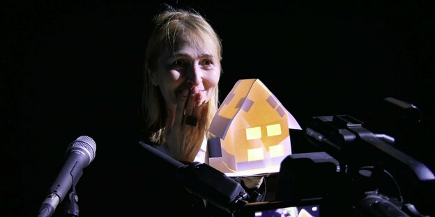 Das Gesicht einer lächelnden Frau hinter einem kleinen Musterhaus, das von innen leuchtet