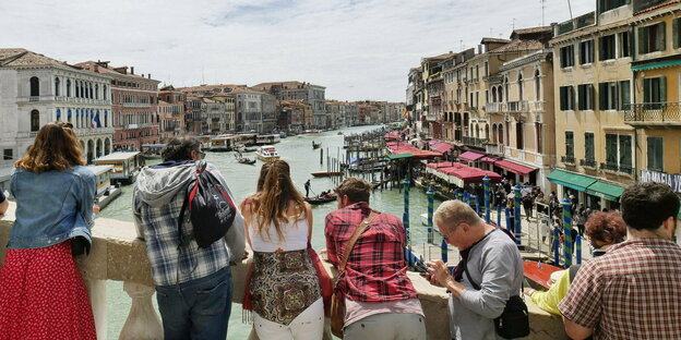 Touristen stehen auf der Rialtobrücke in Venedig und blicken auf den Canal Grande.
