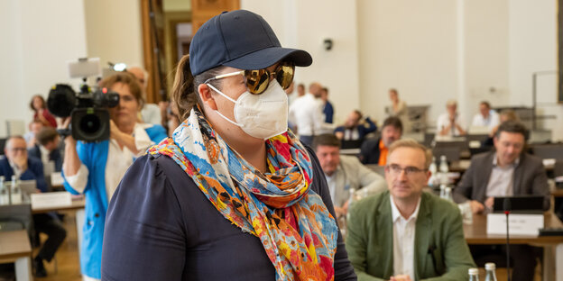 Eine Frau mit Maske steht in einem Gerichtssaal.