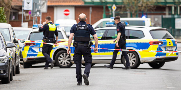 Auf einer Straße in Nienburg parken mehrere Streifenwagen.  Drei uniformierte Polizisten bewegen sich hinter einer Absperrung.