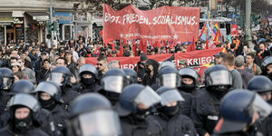 Demonstration mit rotem Front-Banner "Brot, Frieden, Sozialismus". Davor behelmte und vermummte Polizisten
