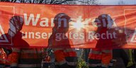 Die Sonne scheint durch ein rotes Banner mit der Aufschrift " Warnstreik - unser gutes Recht", man sieht die Silhouetten von drei Männern in Arbeitskleidung