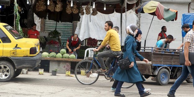 Menschen laufen auf der Straße und fahren Fahrrad, im Hintergrund Marktstände Menschen laufen auf der Straße und fahren Fahrrad, im Hintergrund Marktstände