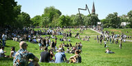 Menschen sitzen bei sonnigem Wetter auf einer Grünfläche, dem Görlitzer Park. Im Hintergrund eine Kirche.