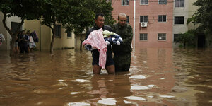 Ein Mann, der ein Baby trägt, watet durch eine überschwemmte Straße.