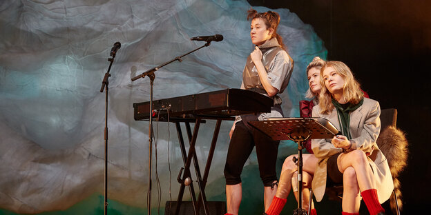 Drei Schauspielerinnen sitzen hinter einem Keyboard und Mikrofonen