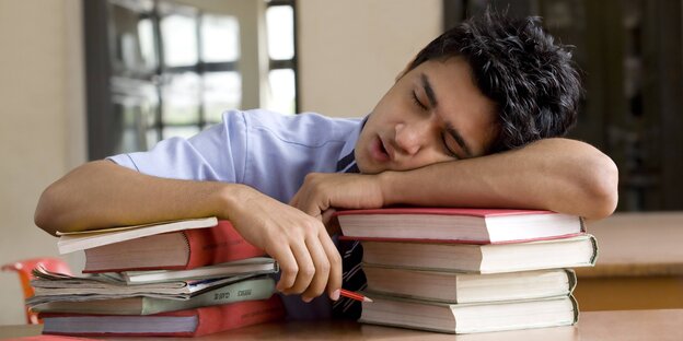 Ein Student schläft auf einem Stapel Bücher Ein Student schläft auf einem Stapel Bücher