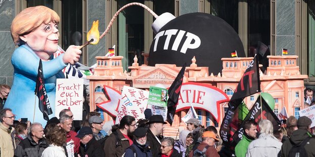 Auf dem vom Karnevalswagenbauer Jacques Tilly gestalteten Skulpturenwagen zündet symbolisch eine Merkel-Figur die ttip-Bombe auf dem Reichstag Auf dem vom Karnevalswagenbauer Jacques Tilly gestalteten Skulpturenwagen zündet symbolisch eine Merkel-Figur die ttip-Bombe auf dem Reichstag