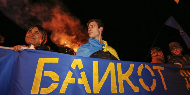 Menschen halten ein blaues Banner, auf dem „Boykott“ auf russisch steht Menschen halten ein blaues Banner, auf dem „Boykott“ auf russisch steht