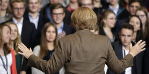 Angela Merkel vor einer Gruppe Menschen, die Arme ausgebreitet