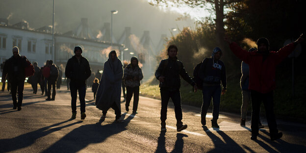 Menschen laufen in der Dämmerung eine Straße entlang Menschen laufen in der Dämmerung eine Straße entlang