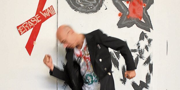 Ein Mann mit Glatze hopst vor einem Bild. Es ist der Maler ter Hell. Ein Mann mit Glatze hopst vor einem Bild. Es ist der Maler ter Hell.
