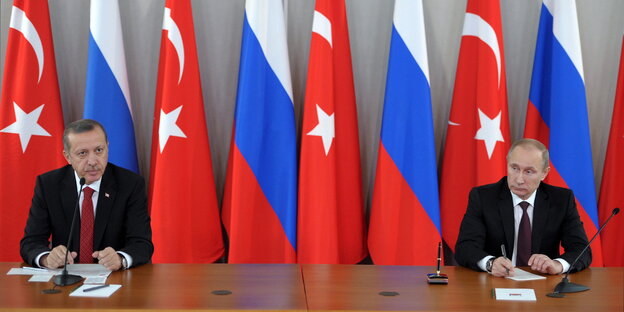 Erdoğan und Putin sitzen weit entfernt an einem Tisch, im Hintergrund Türkei- und Russlandfahnen Erdoğan und Putin sitzen weit entfernt an einem Tisch, im Hintergrund Türkei- und Russlandfahnen