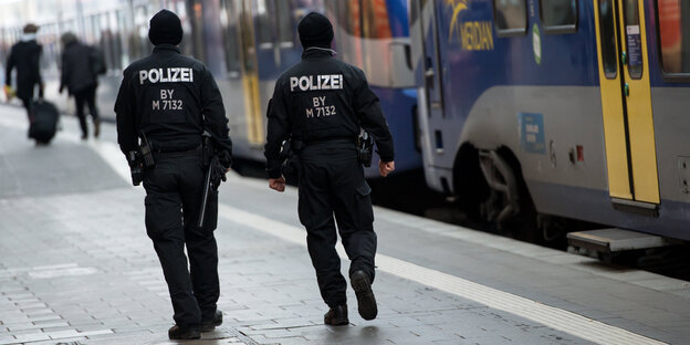 zwei Polizist_innen von hinten laufen an ein paar Bussen vorbei zwei Polizist_innen von hinten laufen an ein paar Bussen vorbei