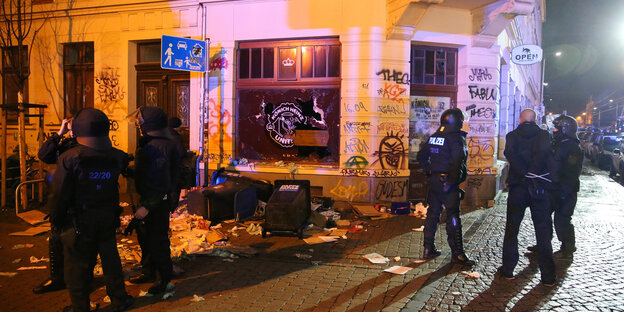 Polizisten stehen am 11.01.2016 im Stadtteil Connewitz in Leipzig vor zerbrochenen Fensterscheiben und verwüsteten Müllcontainern. Polizisten stehen am 11.01.2016 im Stadtteil Connewitz in Leipzig vor zerbrochenen Fensterscheiben und verwüsteten Müllcontainern.