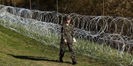 Soldat läuft an Zaun aus Stacheldrahtrollen entlang