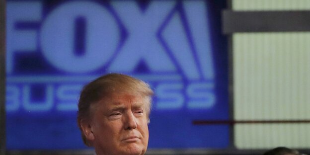 Donald Trump, ein Mann mit blonden Haaren und im Anzug, steht vor einem Schild mit der Aufschrift "Fox" Donald Trump, ein Mann mit blonden Haaren und im Anzug, steht vor einem Schild mit der Aufschrift "Fox"