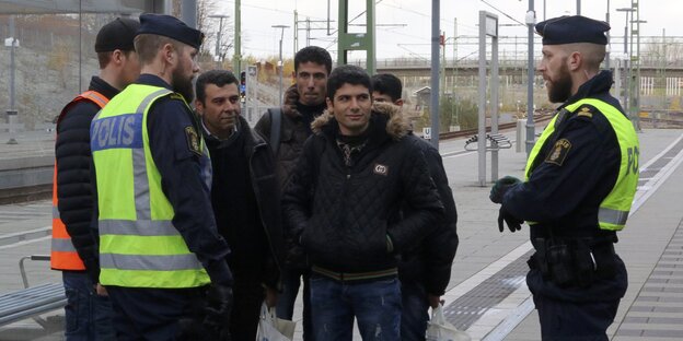 Zwei schwedische Polizisten reden mit einer Gruppe von Männern am Bahnhofsgleis Zwei schwedische Polizisten reden mit einer Gruppe von Männern am Bahnhofsgleis