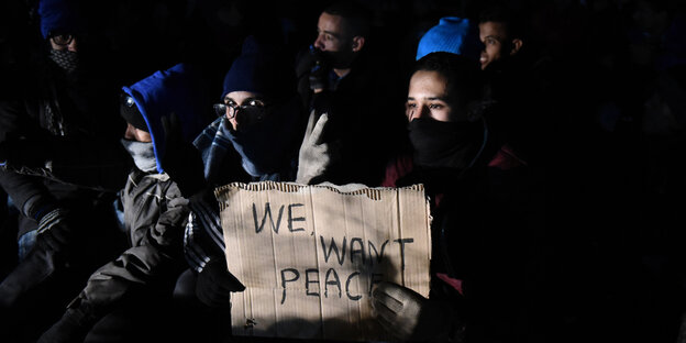 Flüchtlinge halten ein sTück Pappe hoch, auf dem steht: "We want peace". Flüchtlinge halten ein sTück Pappe hoch, auf dem steht: "We want peace".