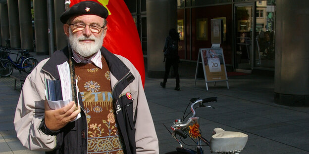 Ein Mann steht neben seinem Fahrrad. Er hat sich eine Flagge über die Schulter gehängt.