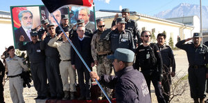 Bundesinnenminister Thomas de Maizière auf einem Podest, umgeben von lokalen Honoratioren und Sicherheitsbeamten. Im Vordergrund schwenkt ein Mann die afghanische Fahne.