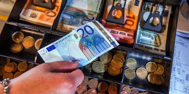 Hand mit 20-Euroschein über geöffneter Registrierkasse Hand mit 20-Euroschein über geöffneter Registrierkasse