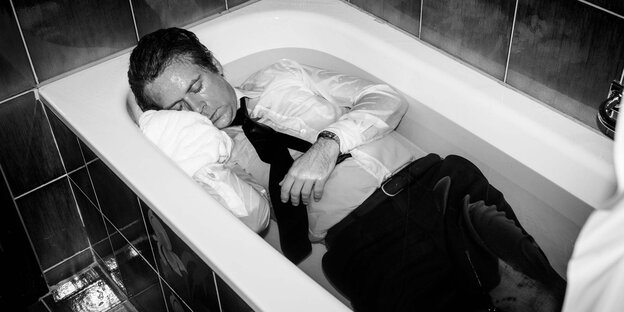 ein Mann liegt angezogen in einer gefüllten Badewanne ein Mann liegt angezogen in einer gefüllten Badewanne