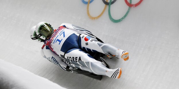 Zwei Doppelsitzrodler aus Korea fahren durch einen Eiskanal, in dem die Olympischen Ringe zu sehen sind.