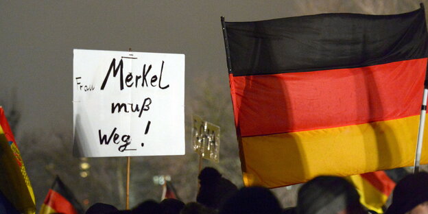Demonstranten halten eine Deutschland-Flagge und ein Schild hoch. Auf dem Schild steht: "Frau Merkel muß weg!" Demonstranten halten eine Deutschland-Flagge und ein Schild hoch. Auf dem Schild steht: "Frau Merkel muß weg!"