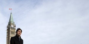 Justin Trudeau vor im scharzen Mantel vor einem Turm und einem weiten, leeren, blau-weißen Himmel