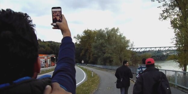 Ein Mensch macht ein Selfie von sich und anderen. Im Hintergrund ein Fluss und eine Brücke. Ein Mensch macht ein Selfie von sich und anderen. Im Hintergrund ein Fluss und eine Brücke.