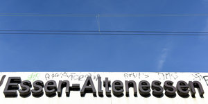 Das S-Bahnschild von Essen-Altenessen, darüber ist der blaue Himmel zu sehen.